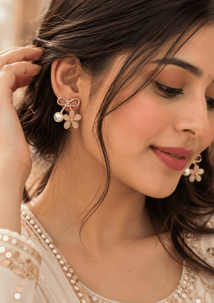 Woman wearing gold tone bow flower pearl drop earrings